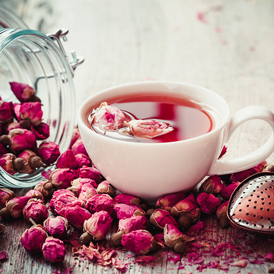 Rose buds tea, tea cup, strainer and glass jar with rosebuds. Selective focus.